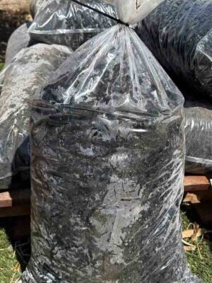 Multiple black mulch bags wrapped in clear plastic, stacked on wooden pallets in an outdoor nursery setting