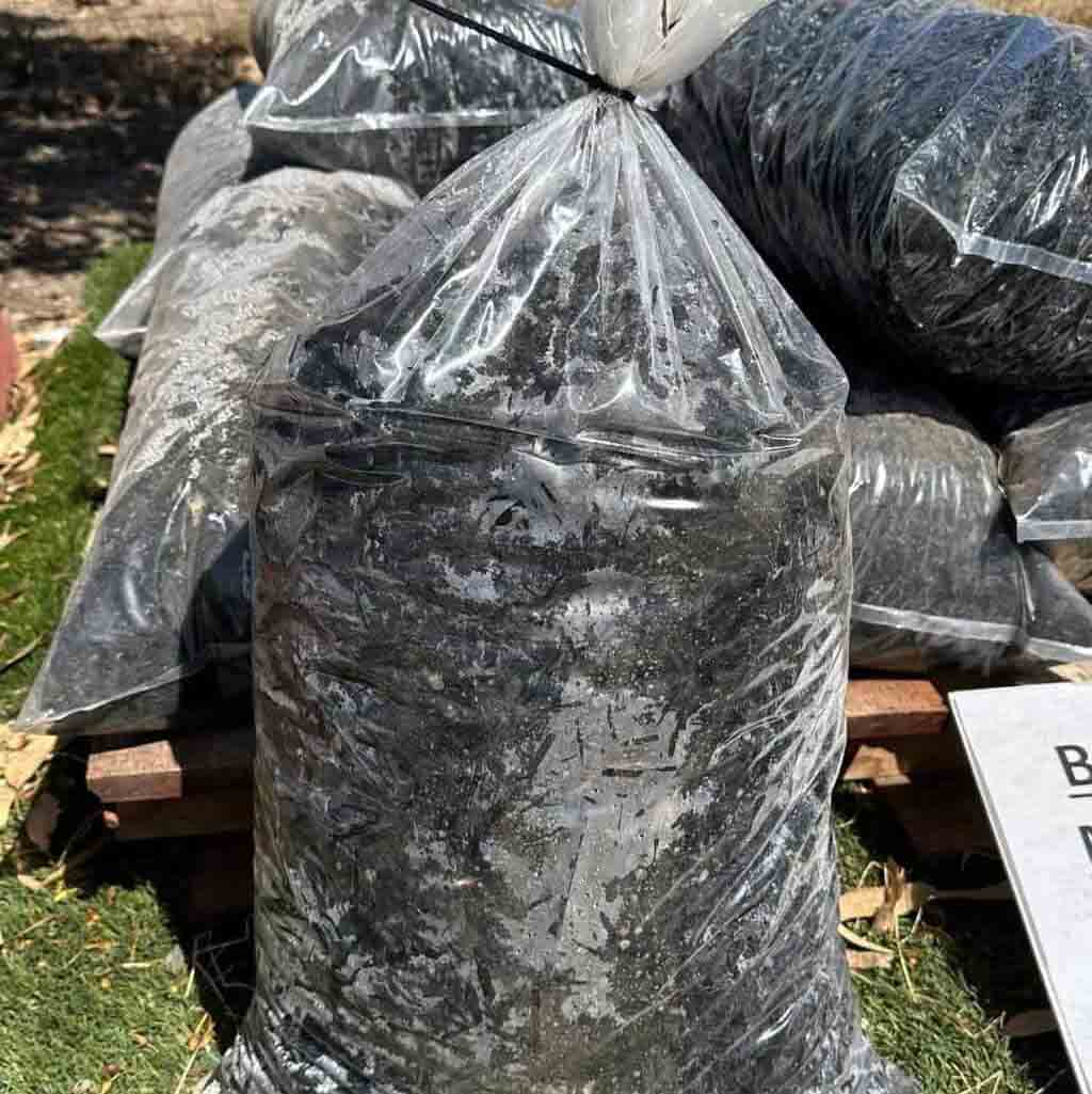 Multiple black mulch bags wrapped in clear plastic, stacked on wooden pallets in an outdoor nursery setting